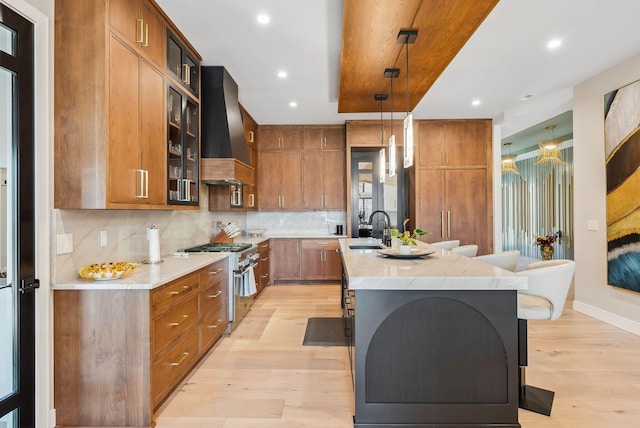 kitchen featuring light wood-type flooring, a center island with sink, high end stainless steel range, brown cabinetry, and custom exhaust hood