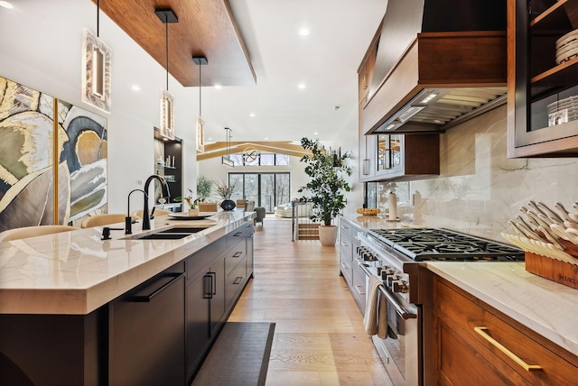 kitchen with high end stainless steel range, custom range hood, a sink, light stone counters, and light wood-style floors