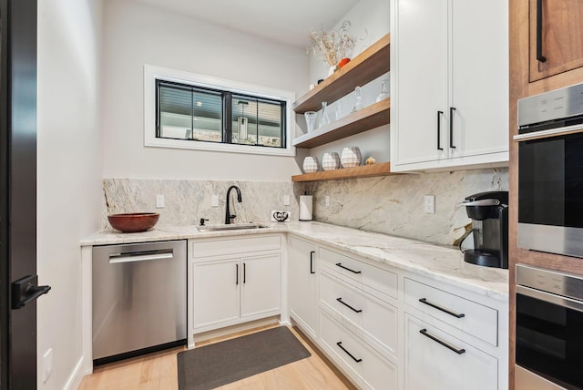 kitchen with a sink, light stone counters, open shelves, tasteful backsplash, and stainless steel appliances