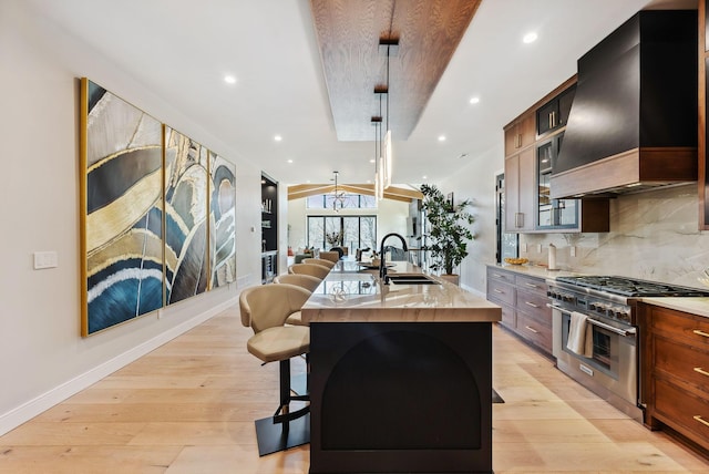 kitchen with light wood-type flooring, custom range hood, a sink, stainless steel stove, and light countertops