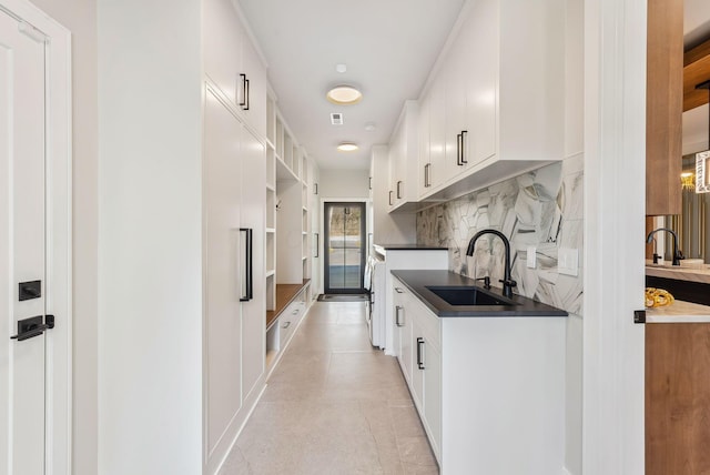 kitchen with dark countertops, decorative backsplash, white cabinets, and a sink