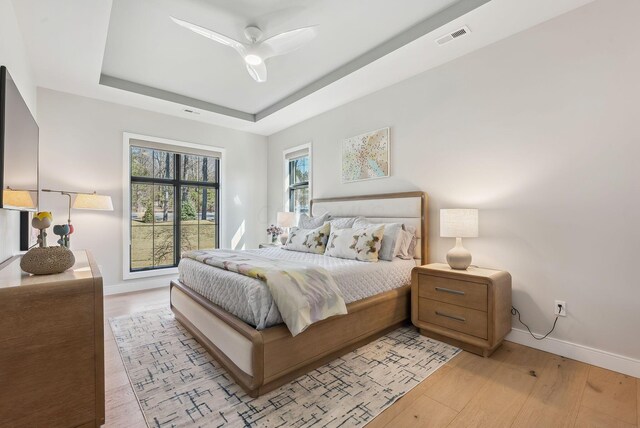 bedroom featuring a raised ceiling, light wood-style floors, visible vents, and baseboards