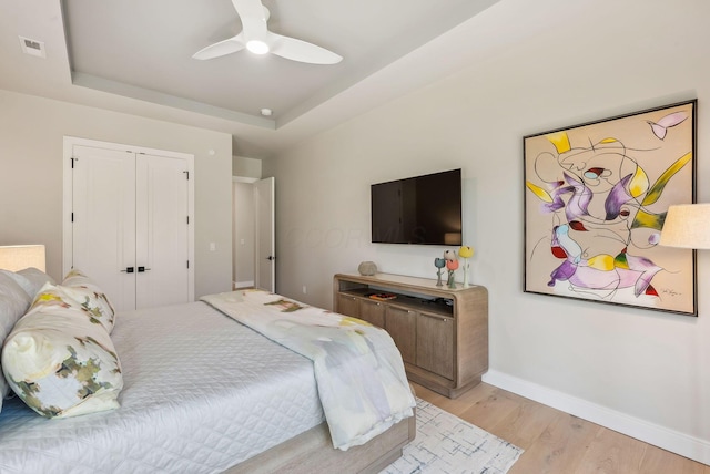 bedroom with visible vents, ceiling fan, baseboards, a tray ceiling, and light wood-style floors