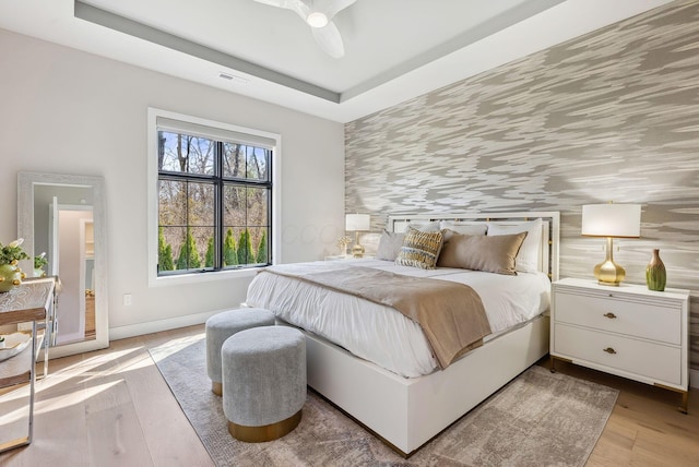 bedroom with visible vents, a raised ceiling, light wood-style floors, and an accent wall