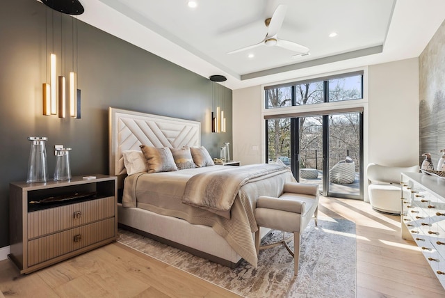 bedroom with a tray ceiling, light wood finished floors, visible vents, and access to outside