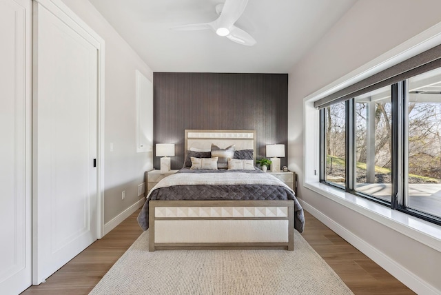 bedroom with a ceiling fan, an accent wall, baseboards, and wood finished floors