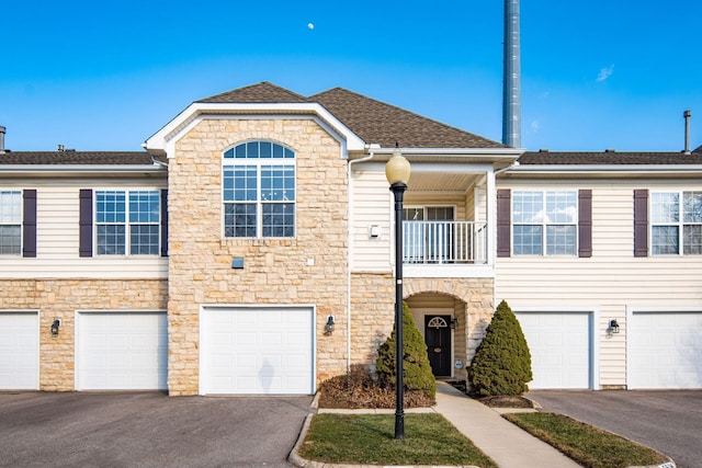 view of property featuring a balcony, a garage, driveway, and roof with shingles