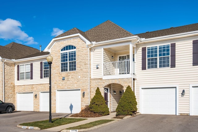 multi unit property with stone siding, a balcony, a shingled roof, and a garage