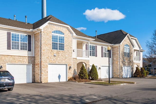 view of front of house with a balcony, an attached garage, driveway, and roof with shingles