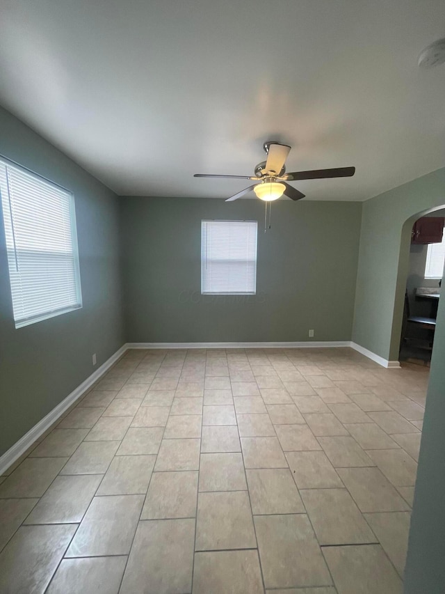 unfurnished room featuring arched walkways, ceiling fan, baseboards, and light tile patterned flooring