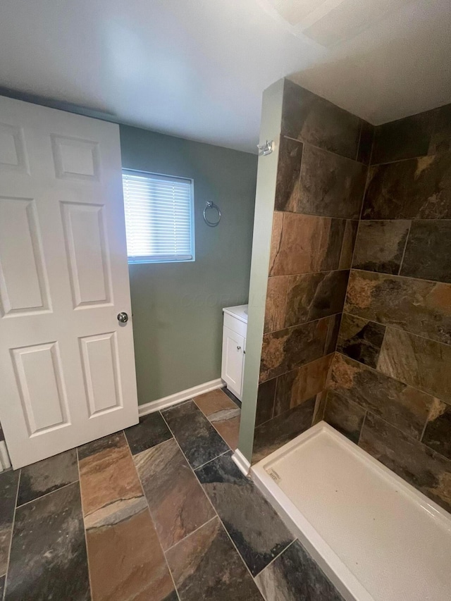 bathroom with baseboards, stone tile flooring, vanity, and a tile shower