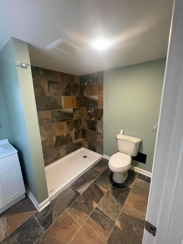 full bath featuring toilet, baseboards, a tile shower, and stone tile flooring