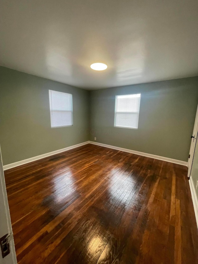 spare room with baseboards and dark wood-type flooring