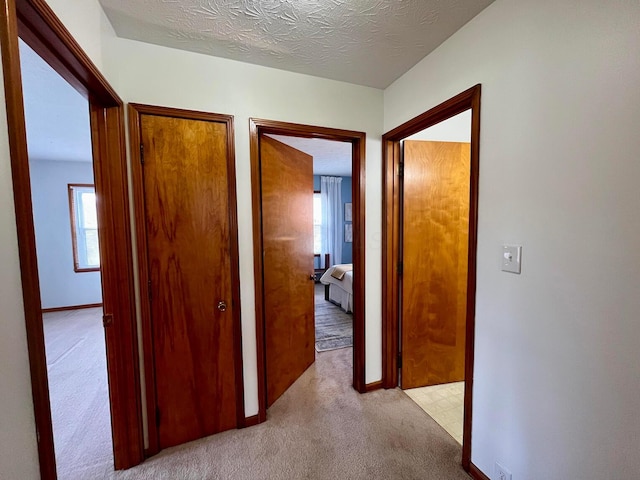 hallway featuring light carpet, a textured ceiling, and baseboards