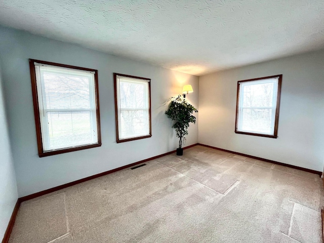 unfurnished room with visible vents, baseboards, light colored carpet, and a textured ceiling