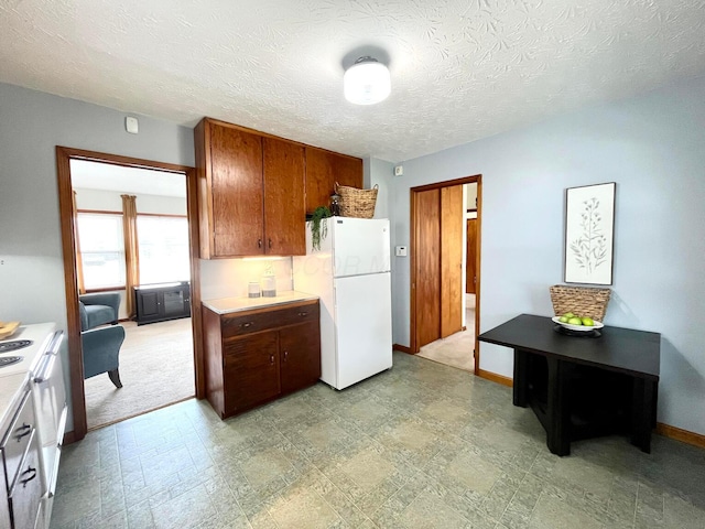 kitchen featuring baseboards, light countertops, freestanding refrigerator, stove, and a textured ceiling