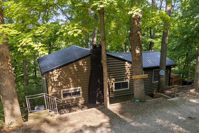 exterior space featuring a standing seam roof, a chimney, log veneer siding, and metal roof