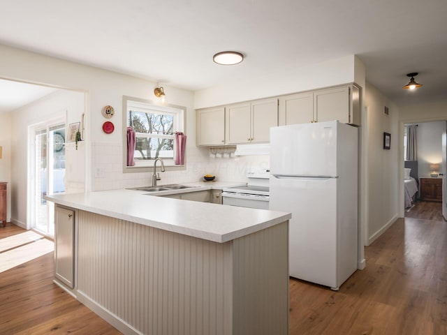 kitchen featuring white appliances, wood finished floors, a peninsula, a sink, and light countertops