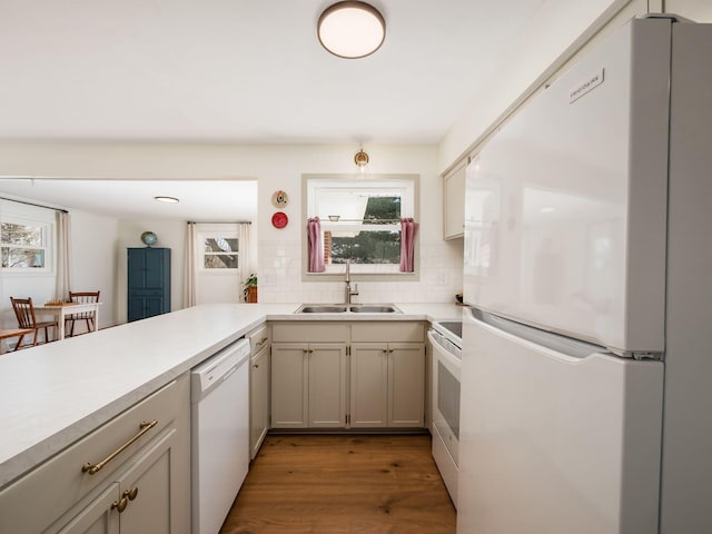 kitchen featuring light wood finished floors, a sink, white appliances, light countertops, and decorative backsplash