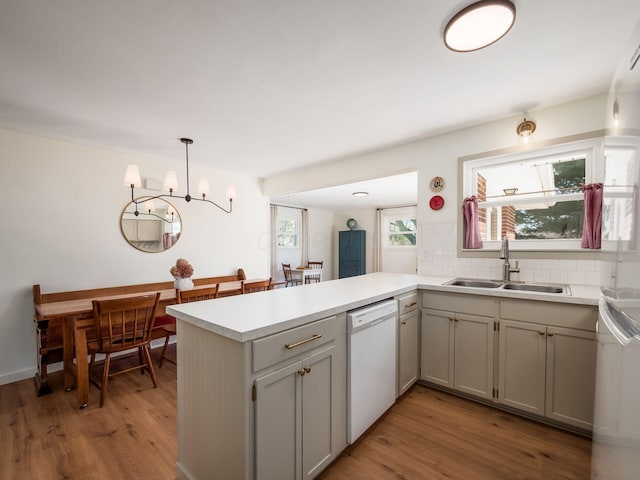 kitchen featuring a sink, tasteful backsplash, light wood-style floors, a peninsula, and dishwasher