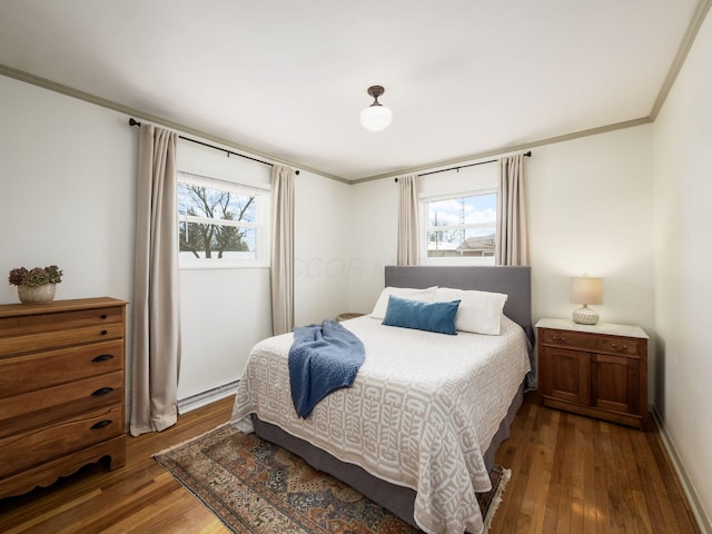 bedroom featuring baseboard heating, multiple windows, ornamental molding, and wood finished floors