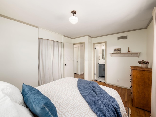 bedroom featuring baseboards, visible vents, ensuite bath, light wood-style flooring, and ornamental molding