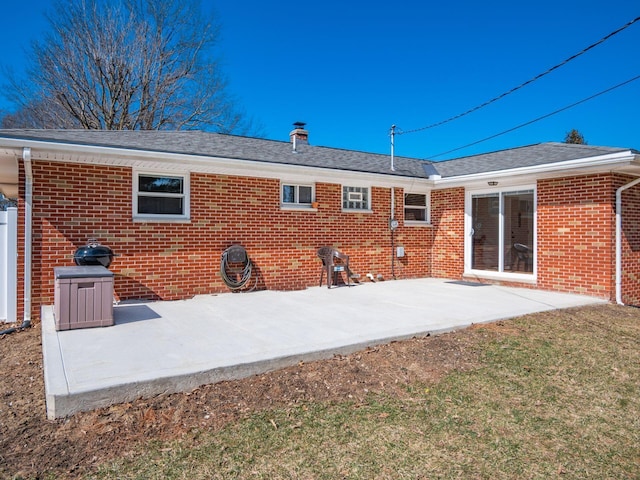 back of house with brick siding, a patio area, a lawn, and roof with shingles