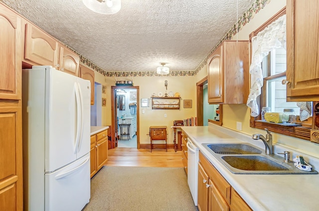 kitchen featuring baseboards, light countertops, white appliances, a textured ceiling, and a sink