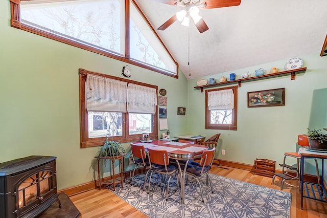 dining space featuring baseboards, a ceiling fan, wood finished floors, and a wood stove