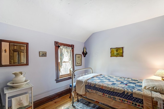 bedroom with wood-type flooring, baseboards, and vaulted ceiling