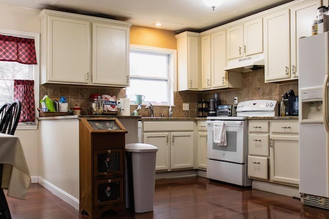 kitchen with white appliances, dark stone counters, recessed lighting, under cabinet range hood, and tasteful backsplash