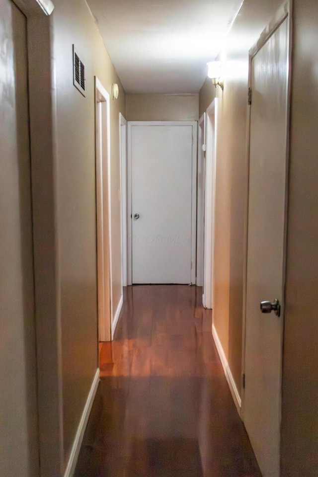 hallway featuring wood finished floors, baseboards, and visible vents