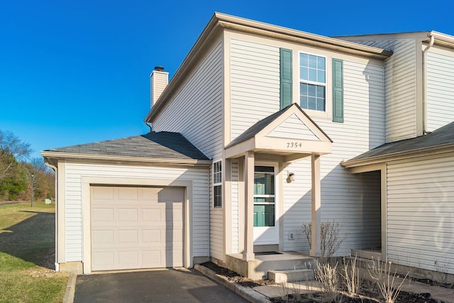 traditional home with aphalt driveway, a chimney, an attached garage, and a shingled roof