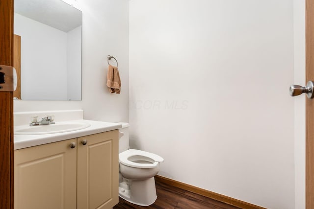 half bathroom featuring toilet, vanity, baseboards, and wood finished floors