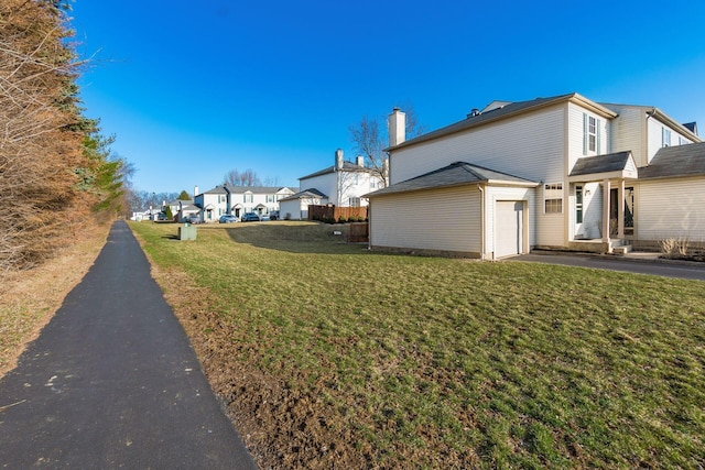 view of side of property featuring aphalt driveway, a yard, a residential view, an attached garage, and a chimney