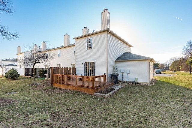 back of property with a chimney, a wooden deck, a yard, and fence