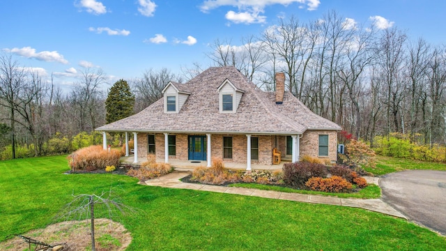 view of front of home featuring brick siding, a porch, a chimney, and a front yard