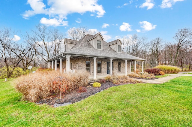 country-style home featuring brick siding, covered porch, a front lawn, and roof with shingles