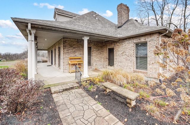 back of property with a shingled roof, brick siding, and a chimney