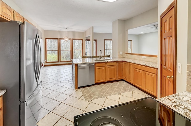 kitchen featuring light stone countertops, a peninsula, a sink, hanging light fixtures, and stainless steel appliances