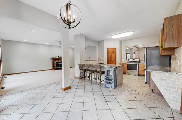 kitchen with a breakfast bar area, light stone counters, baseboards, a fireplace, and appliances with stainless steel finishes