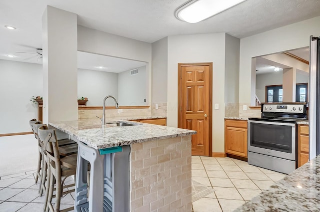 kitchen featuring light tile patterned floors, light stone countertops, a peninsula, stainless steel range with electric stovetop, and tasteful backsplash