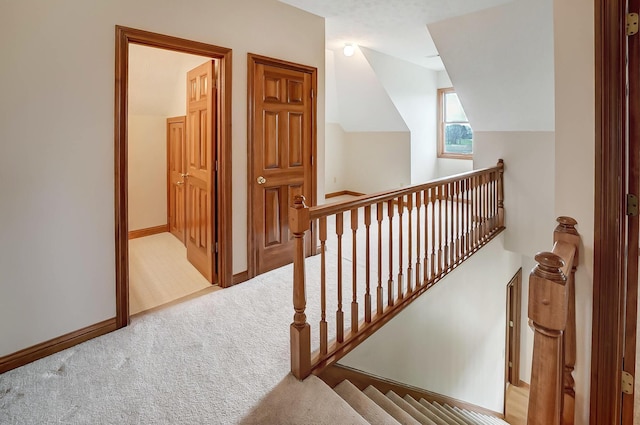 hall with baseboards, carpet floors, lofted ceiling, and an upstairs landing