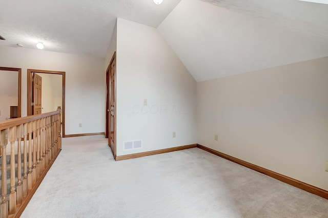 additional living space with vaulted ceiling, baseboards, visible vents, and light carpet