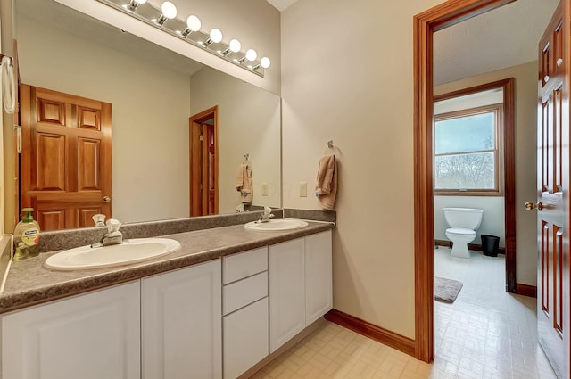 bathroom featuring double vanity, toilet, baseboards, and a sink