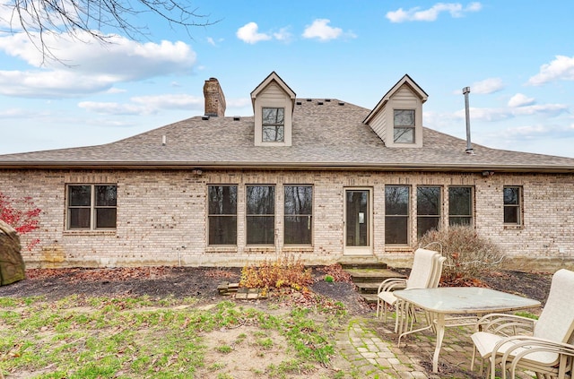 rear view of house with a chimney, a patio area, brick siding, and a shingled roof