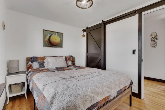 bedroom featuring baseboards, light wood-type flooring, and a barn door