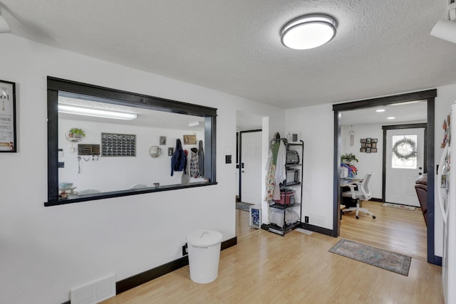 foyer with visible vents, baseboards, a textured ceiling, and wood finished floors