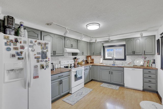 kitchen with white appliances, a sink, gray cabinetry, under cabinet range hood, and light wood-type flooring