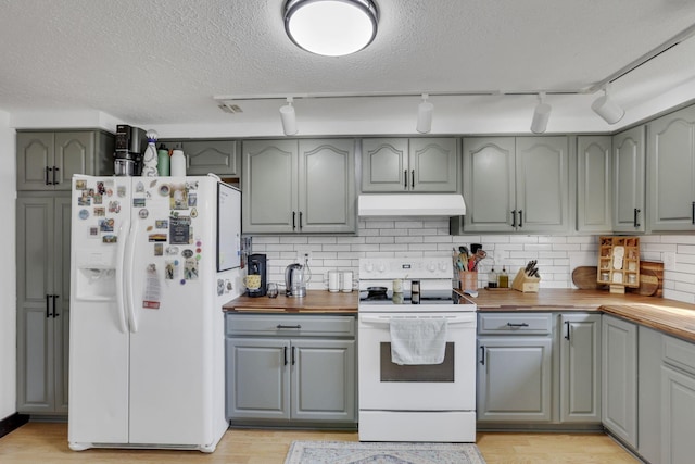 kitchen featuring white appliances, gray cabinets, decorative backsplash, under cabinet range hood, and wood counters